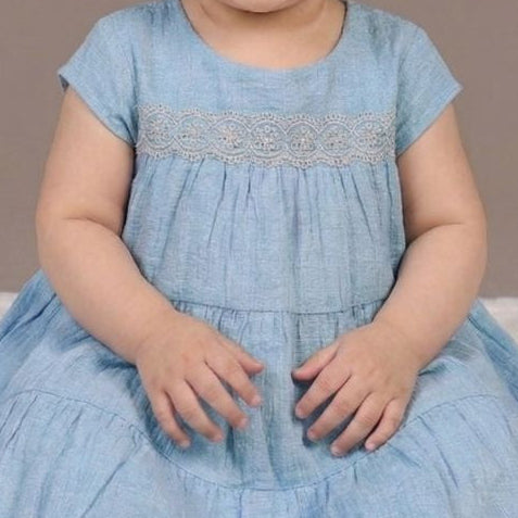Child wearing a blue dress sitting on a white surface with a brown background