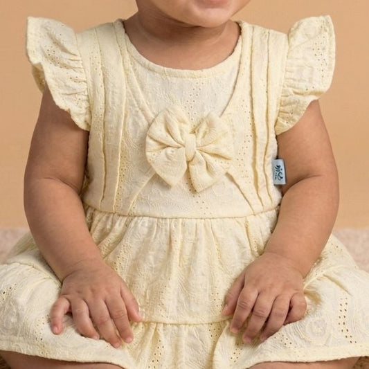 Baby in a yellow dress sitting on a beige surface with a beige background