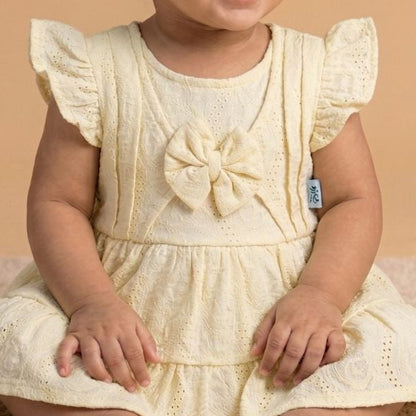 Baby in a yellow dress sitting on a beige surface with a beige background